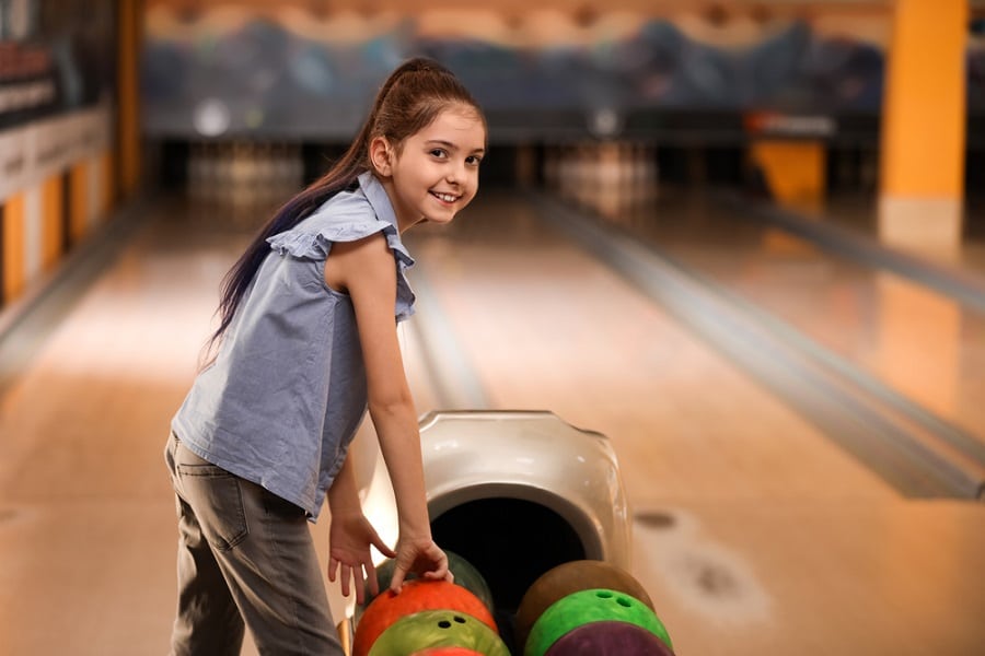 Little girl near balls in bowling club. Space for text